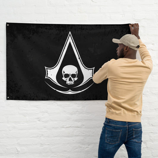 A man from behind hangs a black flag with a white skull and the Assassin's Creed logo on a white brick wall.