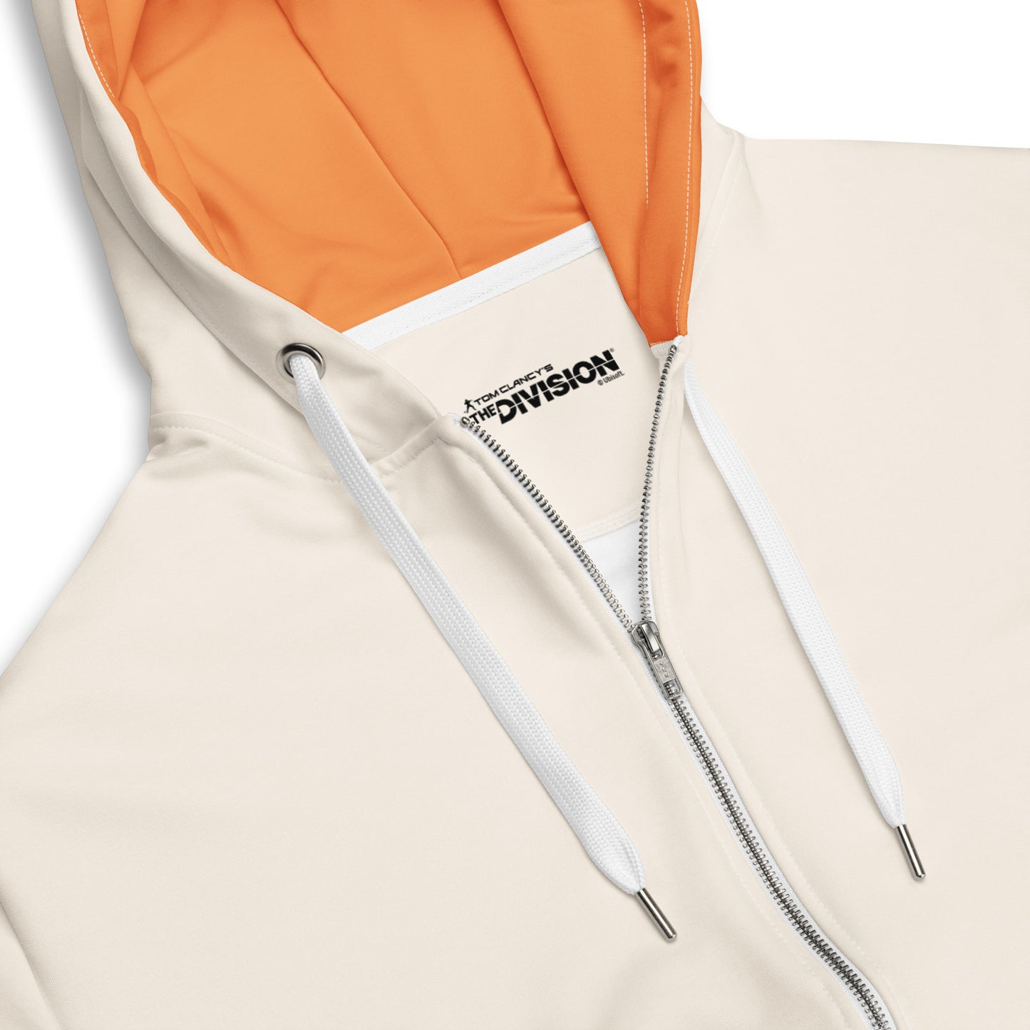 Close-up of a cream zippered hoodie. Features orange hood lining, white drawstrings with metal tips, and "The Division" game
