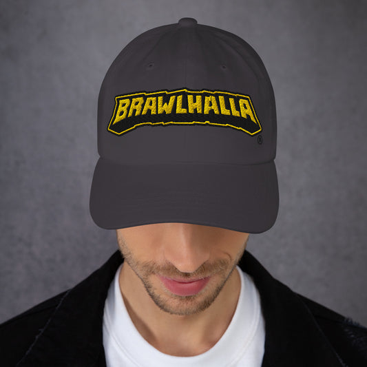 A person wears a dark grey baseball cap with a yellow 'BRAWLHALLA' logo, partially obscuring their face.
